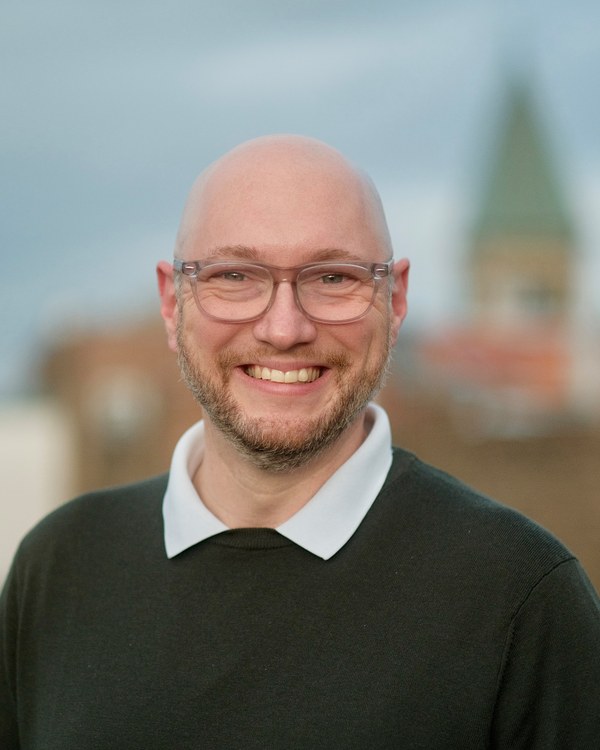 Tobias Treppmann, photographed on a Berlin rooftop, a church tower out of focus behind him